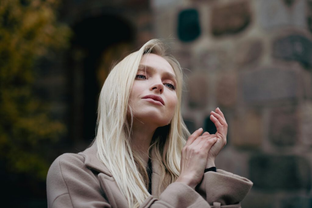 Portrait of a blonde woman standing outdoors against a stone wall, showcasing elegance and confidence.