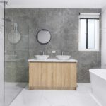 A sleek and stylish modern bathroom with minimalist design, featuring dual washbasins, marble tiles, and a glass shower enclosure.