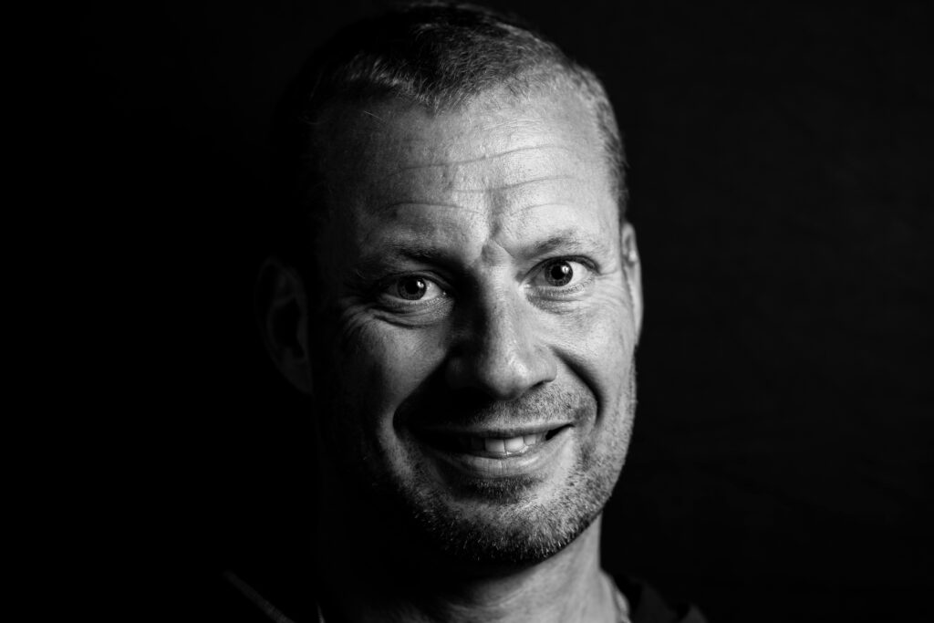 Monochrome close-up portrait of a smiling man with distinct lighting.